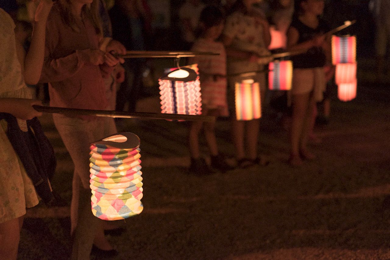 Des enfants et des adultes portent des lanternes en papier par une chaude soirée d’été