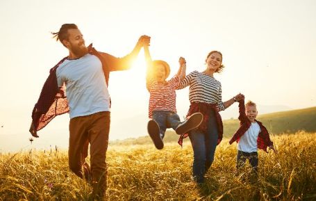 Une famille avec papa, maman et deux enfants courent dans les champs au coucher du soleil