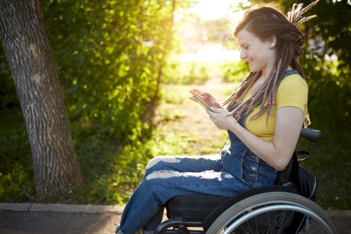 Dans un jardin, une adolescente, en salopette bleue avec des dreadlocks et en fauteuil roulant, partage des SMS avec son chéri. C’est un moment de plaisir, elle sourit.
